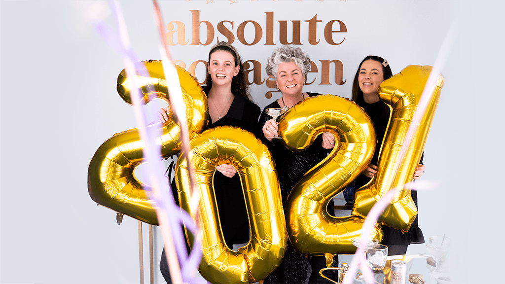 Photo showing Maxine, Margot and Darcy Laceby cheering and holding large gold 2021-shaped balloons while confetti falls around them